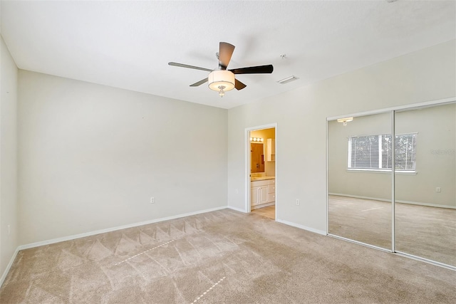 unfurnished bedroom featuring ceiling fan, light colored carpet, ensuite bathroom, and a closet