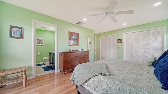 bedroom with ensuite bath, two closets, ceiling fan, and light hardwood / wood-style flooring