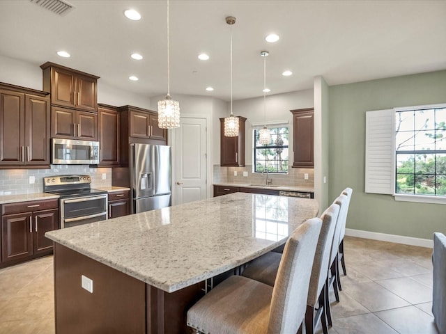 kitchen featuring light stone counters, stainless steel appliances, sink, pendant lighting, and a center island