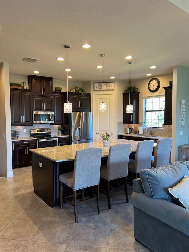 kitchen featuring dark brown cabinetry, a large island, a kitchen breakfast bar, decorative light fixtures, and appliances with stainless steel finishes