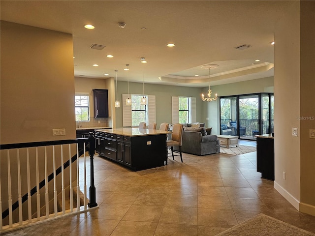 kitchen featuring a center island, an inviting chandelier, a tray ceiling, decorative light fixtures, and a breakfast bar area