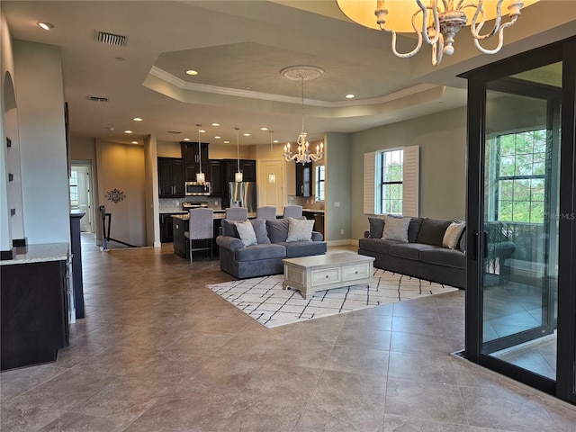 living room featuring a raised ceiling, a chandelier, a healthy amount of sunlight, and ornamental molding