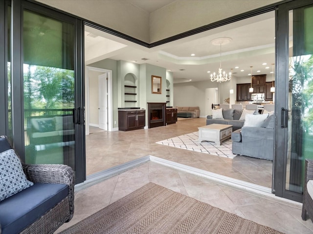 living room with ornamental molding, a chandelier, a raised ceiling, and built in features