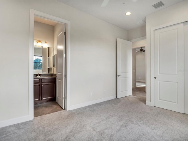 unfurnished bedroom featuring connected bathroom, light carpet, a closet, and ceiling fan