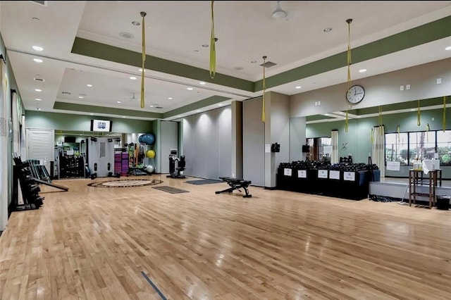 exercise room with light wood-type flooring and a raised ceiling