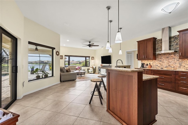 kitchen with a breakfast bar area, tasteful backsplash, ceiling fan, wall chimney range hood, and pendant lighting