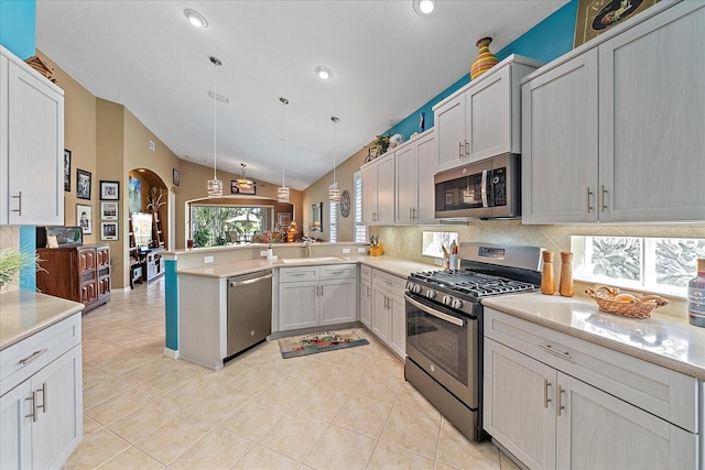 kitchen featuring kitchen peninsula, appliances with stainless steel finishes, light tile patterned floors, decorative light fixtures, and vaulted ceiling