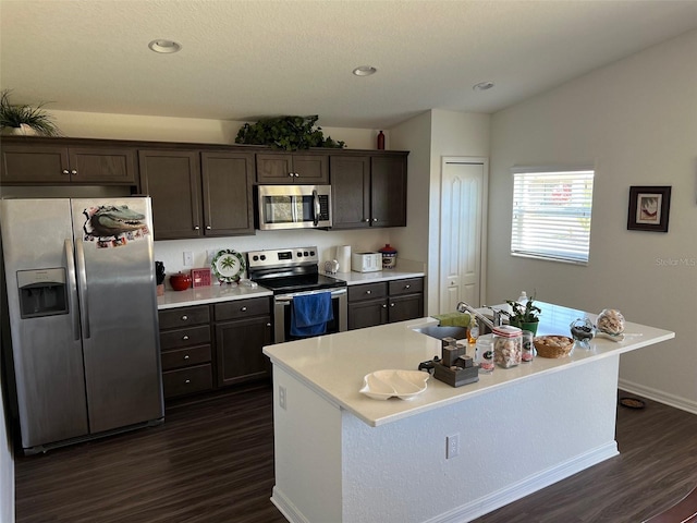 kitchen featuring sink, an island with sink, dark hardwood / wood-style floors, dark brown cabinets, and appliances with stainless steel finishes