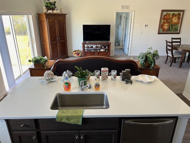 kitchen with stainless steel dishwasher, sink, carpet flooring, and a center island with sink