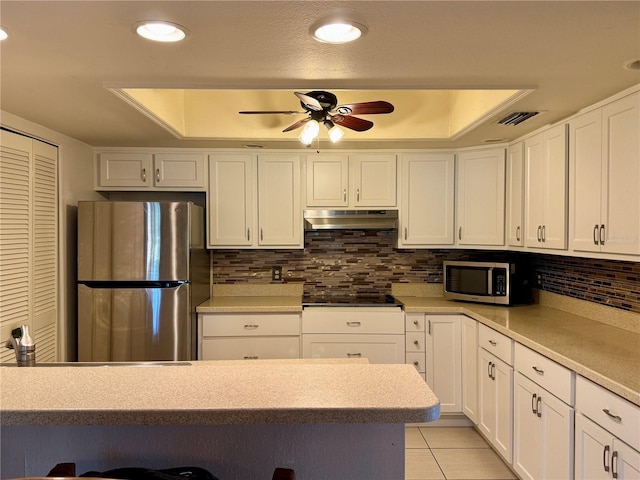 kitchen featuring a raised ceiling, stainless steel appliances, white cabinetry, and ceiling fan