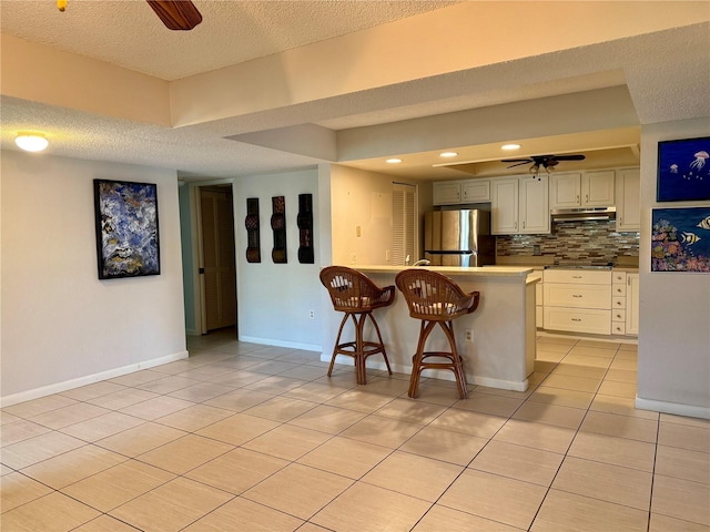 kitchen with ceiling fan, stainless steel appliances, kitchen peninsula, a textured ceiling, and a kitchen bar