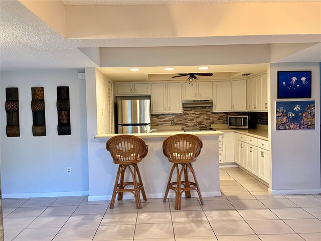 kitchen featuring white cabinets, a kitchen breakfast bar, ceiling fan, a textured ceiling, and appliances with stainless steel finishes