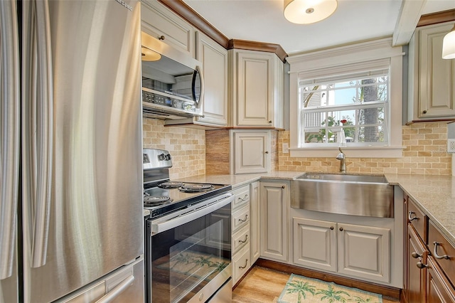 kitchen with light hardwood / wood-style floors, stainless steel appliances, backsplash, light stone counters, and sink