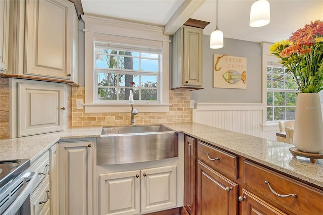 kitchen with light stone counters, sink, hanging light fixtures, and electric range