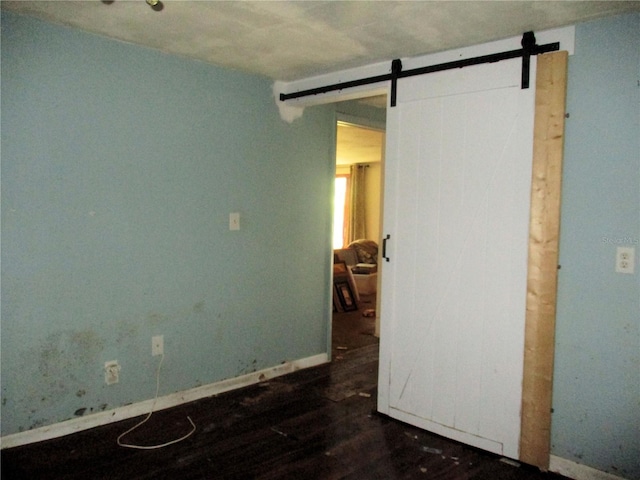 unfurnished room featuring a barn door, wood finished floors, and baseboards