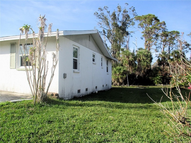 view of side of home with crawl space, stucco siding, and a yard