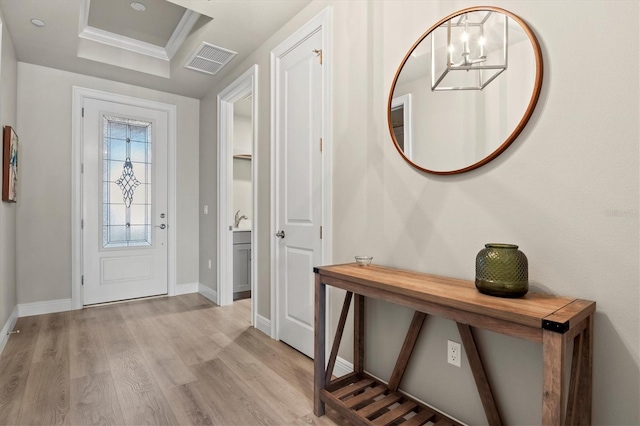 foyer featuring ornamental molding, light hardwood / wood-style floors, a tray ceiling, and an inviting chandelier