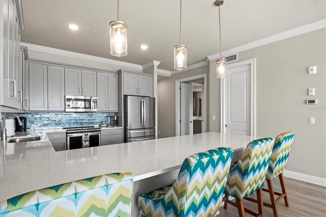 kitchen featuring stainless steel appliances, sink, ornamental molding, a kitchen bar, and pendant lighting