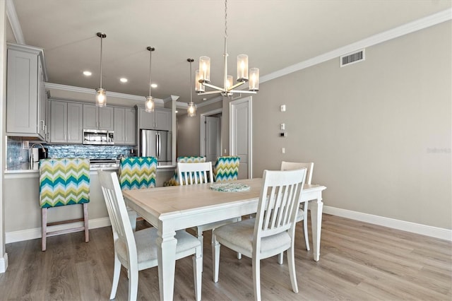 dining space featuring light hardwood / wood-style flooring, a notable chandelier, sink, and crown molding