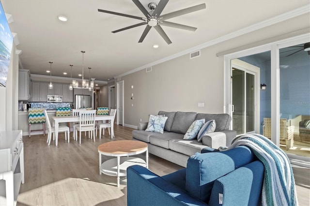 living room with light hardwood / wood-style floors, ceiling fan with notable chandelier, and crown molding