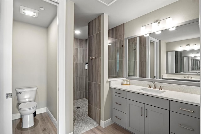 bathroom with hardwood / wood-style floors, vanity, toilet, and tiled shower