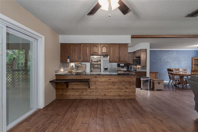 kitchen with ceiling fan, dark wood-type flooring, stainless steel refrigerator with ice dispenser, kitchen peninsula, and a textured ceiling