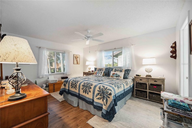 bedroom featuring multiple windows, a textured ceiling, wood finished floors, and a ceiling fan