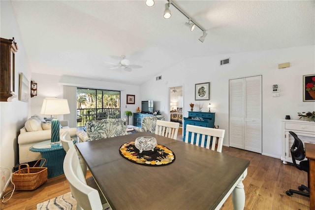 dining space with visible vents, wood finished floors, rail lighting, ceiling fan, and vaulted ceiling