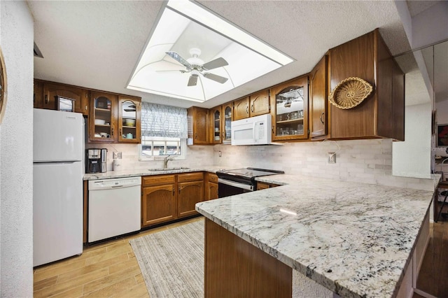 kitchen featuring white appliances, light stone counters, a peninsula, a sink, and brown cabinets