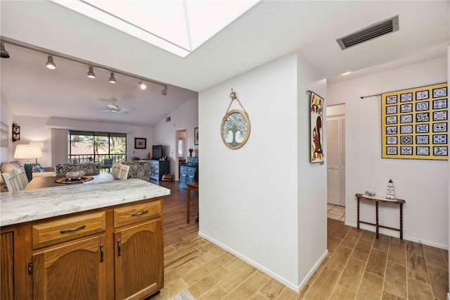 kitchen featuring visible vents, wood finish floors, lofted ceiling with skylight, open floor plan, and a ceiling fan