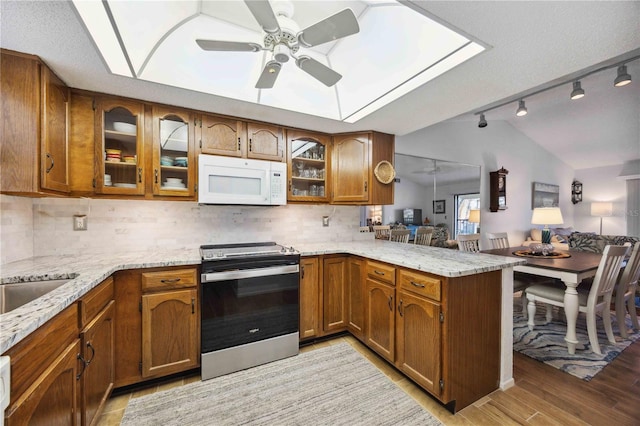 kitchen with brown cabinetry, white microwave, a peninsula, stainless steel electric stove, and tasteful backsplash