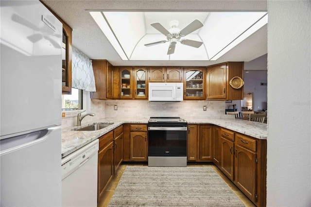 kitchen featuring brown cabinets, a sink, a tray ceiling, white appliances, and a skylight