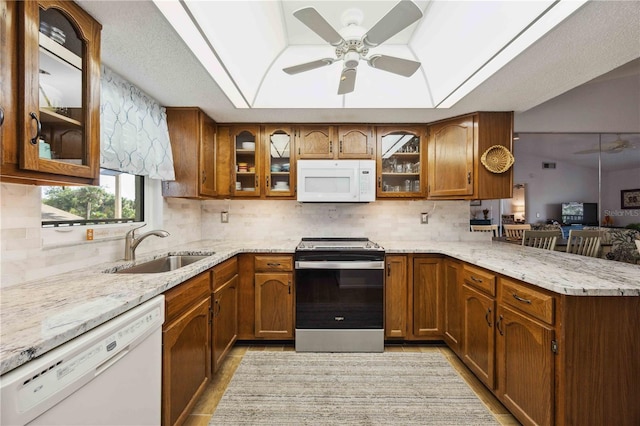 kitchen featuring a tray ceiling, a peninsula, brown cabinetry, white appliances, and a sink