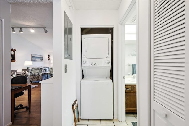 clothes washing area featuring light wood-type flooring, electric panel, stacked washing maching and dryer, a textured ceiling, and a sink