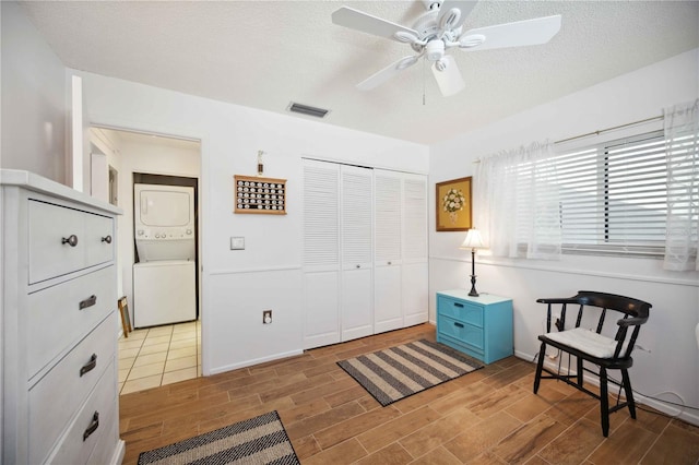 sitting room with visible vents, wood tiled floor, ceiling fan, stacked washer and dryer, and a textured ceiling