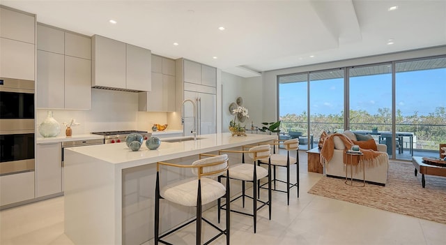 kitchen with appliances with stainless steel finishes, gray cabinets, sink, a breakfast bar area, and a kitchen island with sink