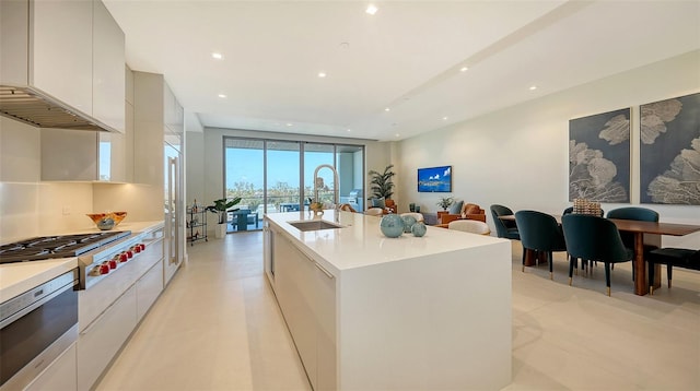 kitchen featuring stainless steel appliances, white cabinetry, sink, an island with sink, and premium range hood