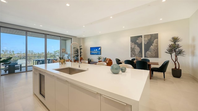 kitchen featuring white cabinetry, a wall of windows, a center island with sink, and sink