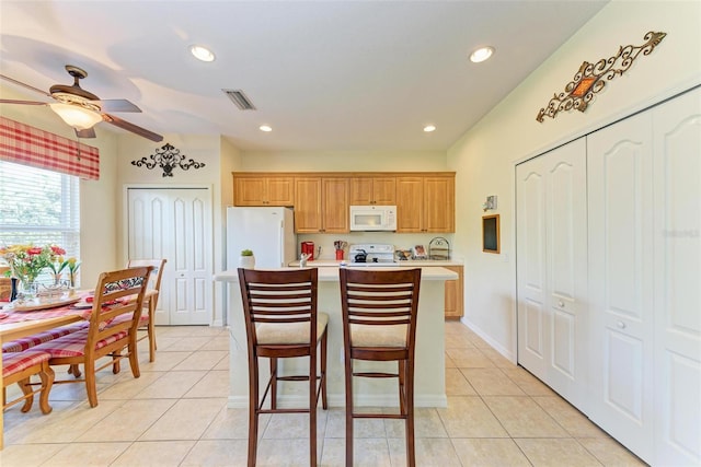 kitchen featuring light tile patterned floors, white appliances, a center island, and ceiling fan