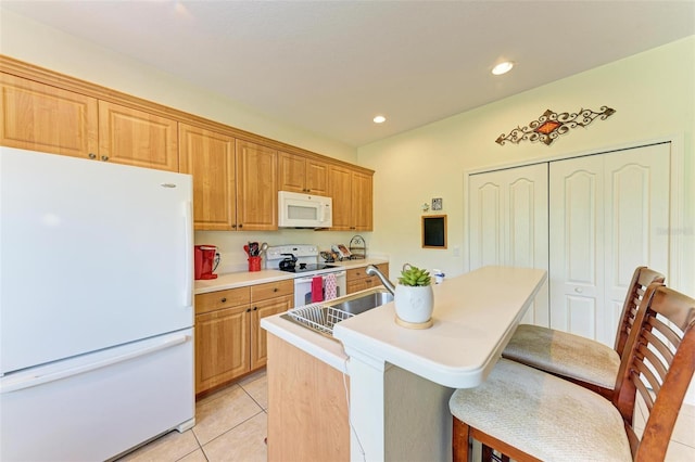 kitchen with white appliances, sink, an island with sink, light tile patterned flooring, and a breakfast bar area