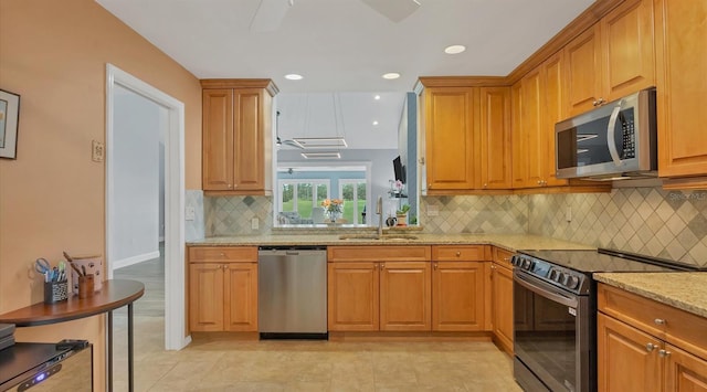 kitchen with stainless steel appliances, light stone counters, tasteful backsplash, and sink