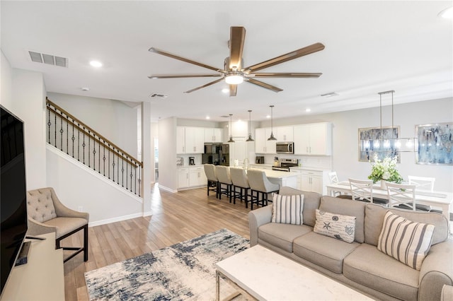 living room with sink, light hardwood / wood-style floors, and ceiling fan with notable chandelier