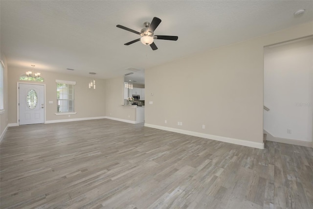 unfurnished living room featuring a textured ceiling, light hardwood / wood-style floors, and ceiling fan with notable chandelier