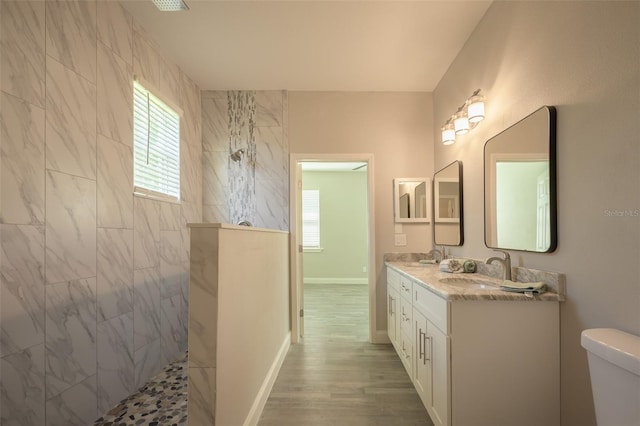 bathroom featuring wood-type flooring, vanity, toilet, and a tile shower