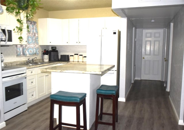 kitchen with white cabinets, a kitchen breakfast bar, white appliances, and backsplash