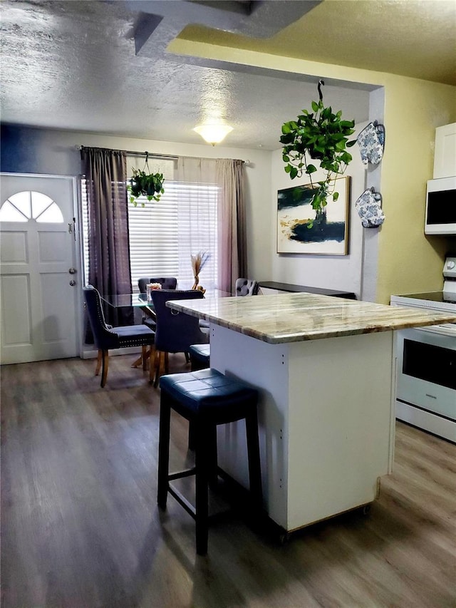 kitchen with dark wood-type flooring, a textured ceiling, white appliances, a breakfast bar area, and white cabinets