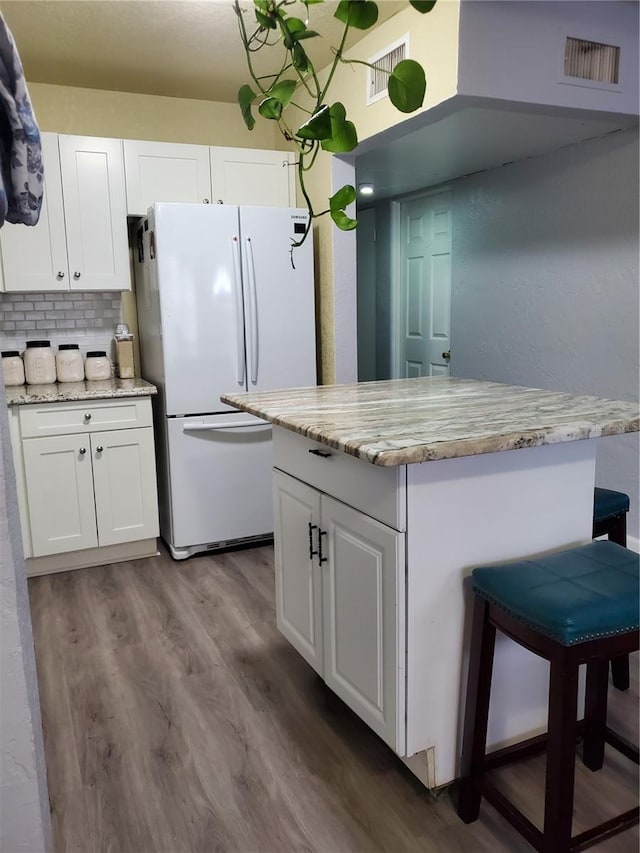 kitchen with tasteful backsplash, white cabinets, hardwood / wood-style floors, and white fridge