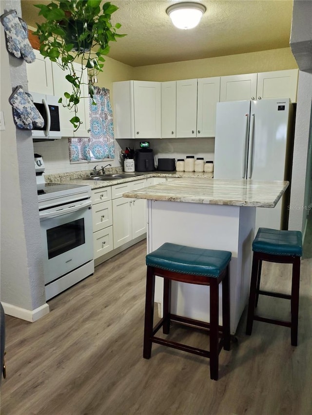 kitchen featuring white cabinetry, light stone counters, hardwood / wood-style floors, white appliances, and a breakfast bar