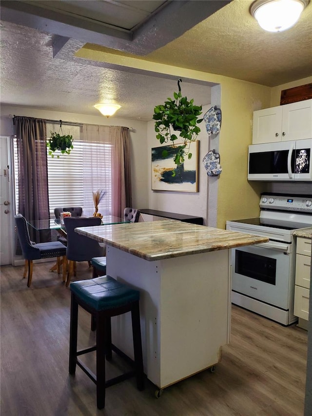 kitchen featuring a center island, white appliances, dark wood-type flooring, a kitchen bar, and white cabinetry