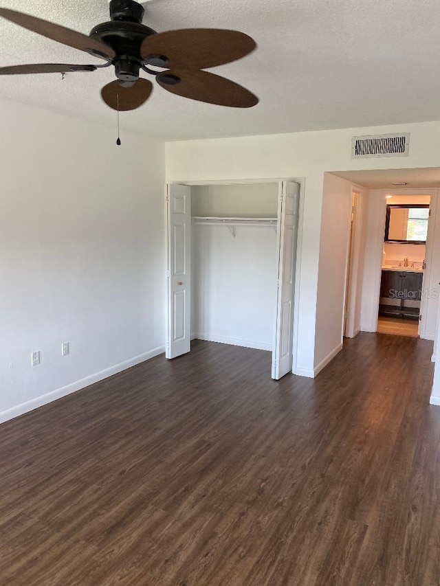 unfurnished bedroom featuring a closet, ceiling fan, a textured ceiling, and dark hardwood / wood-style floors